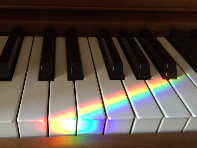 Rainbow piano keys illuminated by a prism beam from the rainbow sundial on the window sill